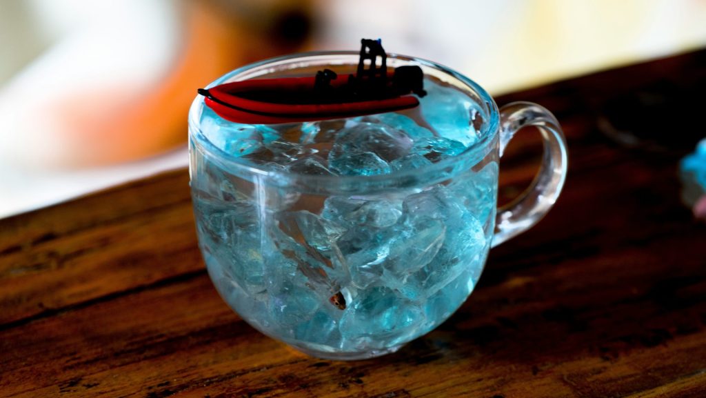A toy boat floats in a glass of ice water.